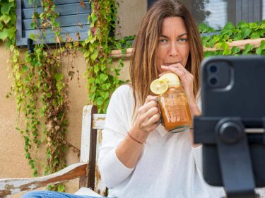 Eine junge Frau macht ein Selfie mit ihrem iPhone, das in einem Stativ vor ihr steht.