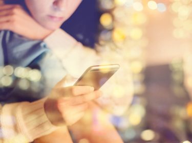 Junge Frau hält ihr iPhone in der Hand, das via iCloud-Backup wiederhergestellt wird.