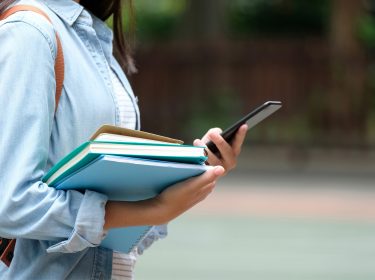 Schülerin mit Smartphone und Büchern