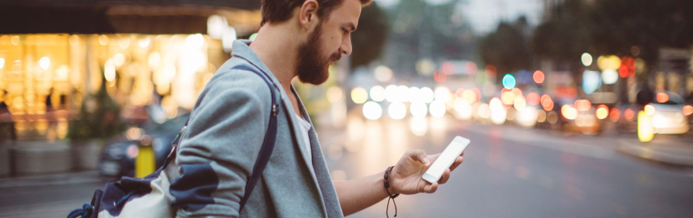 Mann mit Rucksack in der Stadt schaut auf sein Smartphone – V-Multi-Tracker Mann mit Rucksack in der Stadt schaut auf sein Smartphone - V-Multi-Tracker