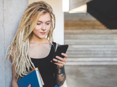 Eine Frau lehnt mit Smartphone in der Hand an einer Wand