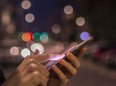 Frau nutzt nachts am Smartphone Google Maps im dunklen Design.