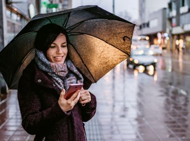 Frau informiert sich am Handy über das Wetter.