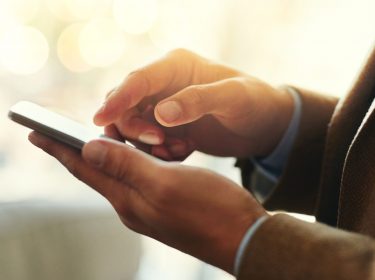 Junger Mann tippt auf das Display seines iPhone 11.