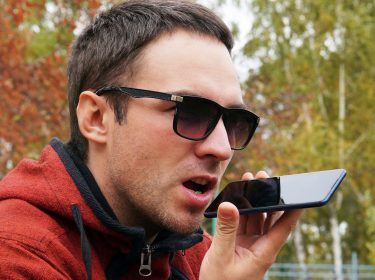 Junger Mann spricht am iPhone mit Siri, um Musik abzuspielen.