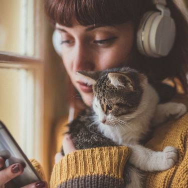 Android 11: So soll der Flugmodus verbessert werden Frau hält Katze im Arm und hört mit ihrem Android-11-Handy Musik.