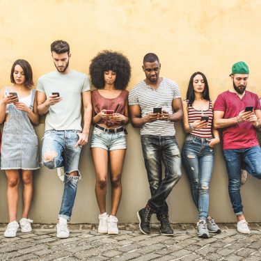 Multiracial friends using smartphone against wall at university college backyard – Young people addicted by mobile smart phone – Technology concept with always connected millennials – Filter image Gruppe von Smartphone-Nutzern
