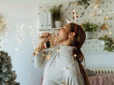 Eine Frau hat sich eine Lichterkette umgelegt und singt zu Musik.