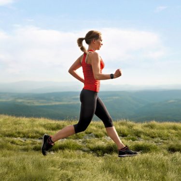 frau-mit-smartwatch-vodafone-onenumber-multisim Eine Frau joggt mit ihrer Smartwatch auf einer Wiese.