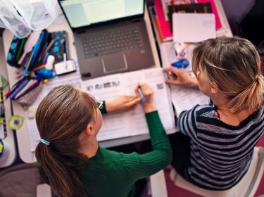 Eine Mutter lernt mit ihrer Tochter am Schreibtisch vor einem Notebook für die Schule.