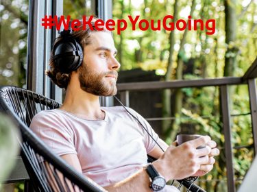 Mann mit Kaffee in der Hand hört über Kopfhörer Mindfulness-Podcasts auf dem Balkon