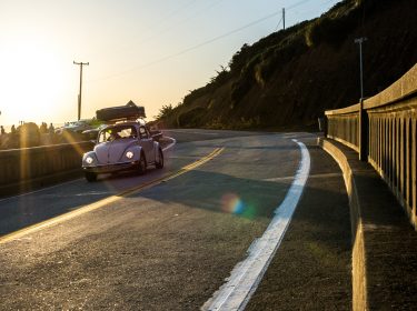In Reise-Dokus fährt ein weißes Auto im Abendlicht auf einer Straße