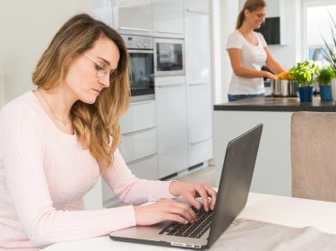 Junge Frau sitzt konzentriert mit Laptop an Tisch in Wohnküche