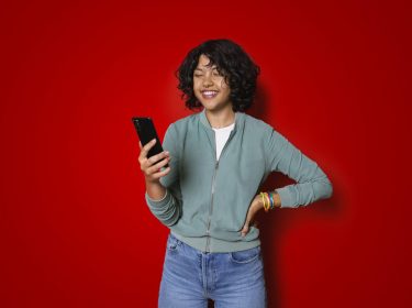 Eine junge Frau schaut lächelnd auf ihr Smartphone während sie die MeinVodafone-App nutzt