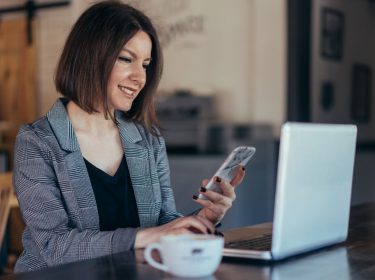 Frau nutzt Smartphone und Laptop.