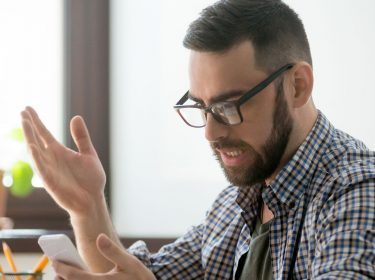 Mann schaut wütend auf sein Smartphone.