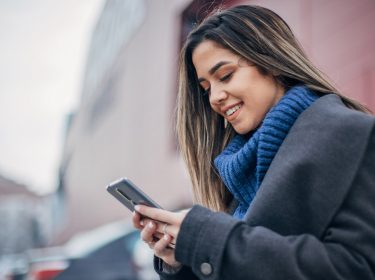 Frau sucht mit dem Smartphone auf einem Parkplatz ihr Auto