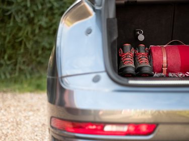 Im Kofferraum eines Autos liegen Wanderschuhe und ein Rucksack, befestigt daran ist der Curve GPS-Tracker von Vodafone.