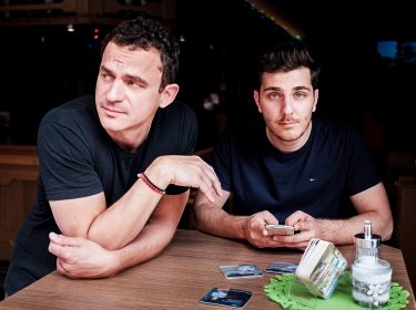 Die Comedy-Autoren Christian Huber und Tarkan Bagci stehen an einem Tisch in einer Kneipe