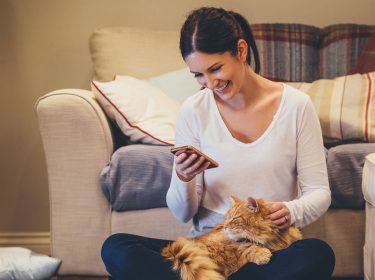 Frau mit Android-Smartphone und Katze auf dem Schoß