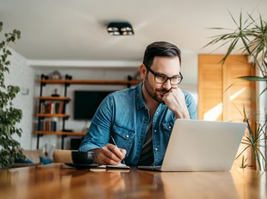 Mann sitzt im Wohnzimmer al Laptop