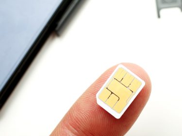 SIM-Karte auf Finger mit Handy im Hintergrund