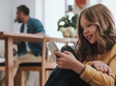 Mädchen mit Smartphone, im Hintergrund der Vater