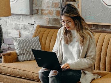 Frau sitzt mit Laptop auf dem Sofa im Wohnzimmer
