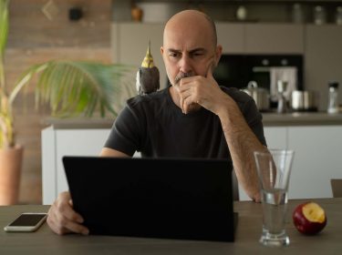 Mann sitzt zu Hause in der Küche am Laptop und grübelt