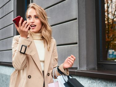 Frau mit Einkaufstüten spricht einen Kurzbefehl für Siri ins iPhone