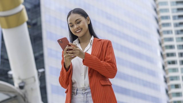 Frau mit rotem Blazer schaut lächelnd auf ihr iPhone.
