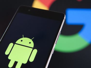 Android-Männchen auf einem Smartphone, Google-Symbol im Hintergrund