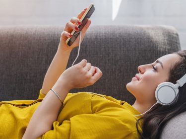 Frau liegt auf dem Sofa und hört mit dem Smartphone Musik