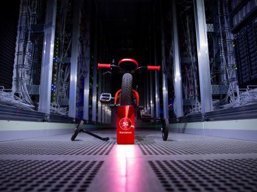 Ein rotes Fahrrad mit Stützrädern, davor ein Smartphone, das 