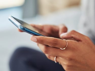 Zwei Hände einer jungen Frau scrollen auf einem Smartphone.