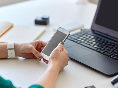 Hände halten Android-Handy vor Laptop