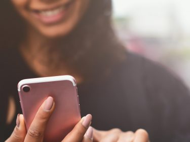 Lachende Frau hält iPhone in Rosegold – iOs 15 Rückblicke