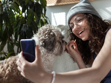 Eine Frau macht ein Foto von sich und ihrem Hund per Smartphone.