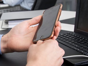 Mann schließt sein iPhone ans Ladekabel an, da der Akku leer ist.