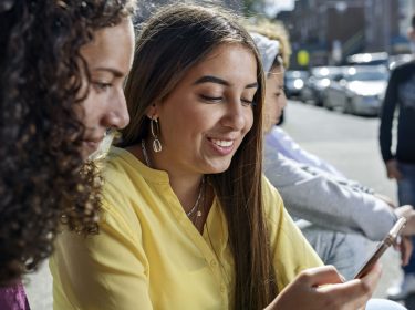 Zwei junge Frauen gucken draußen auf ein iPhone