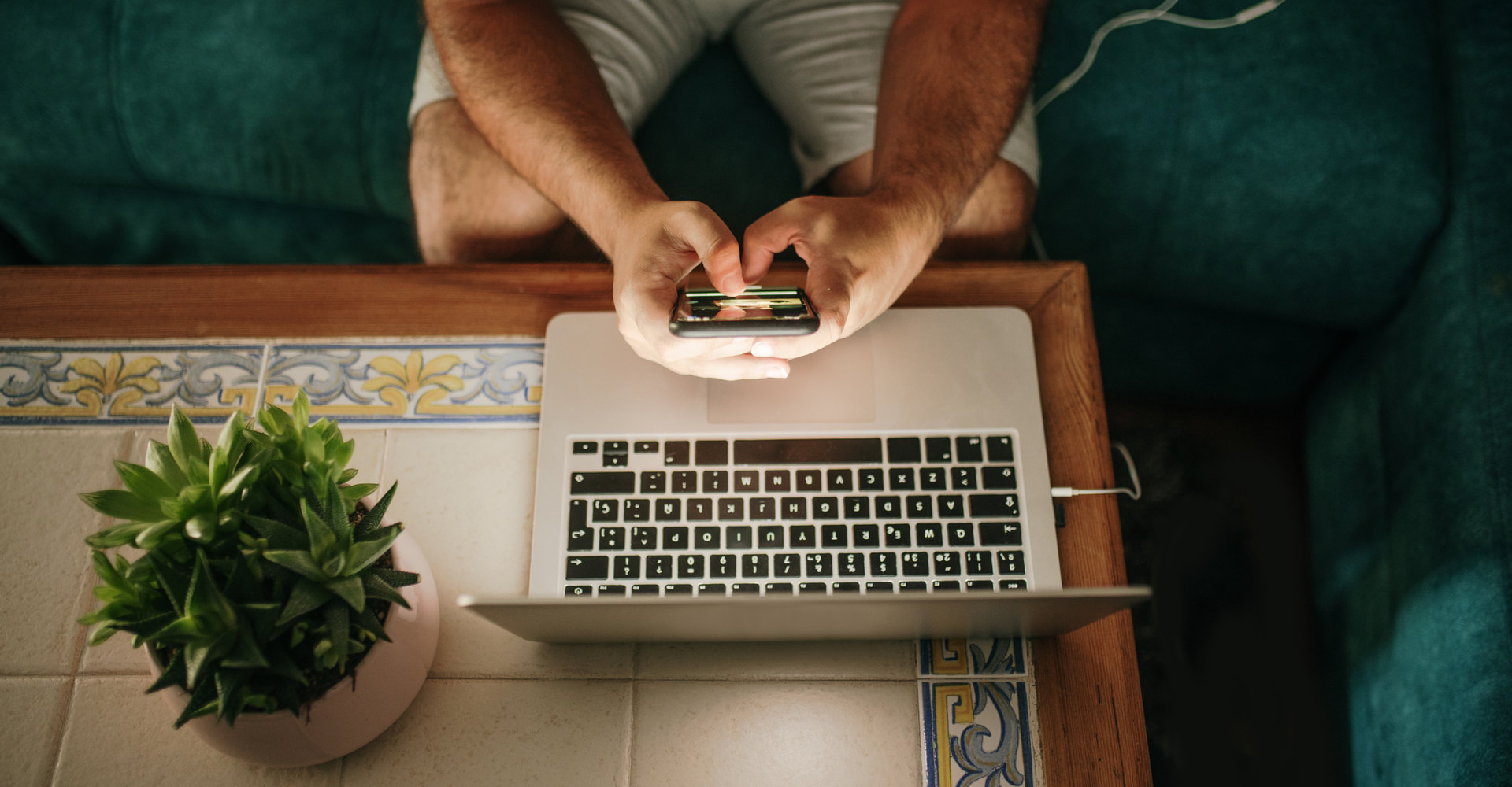 Mann sitzt mit Smartphone am Laptop