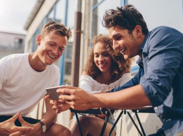 Eine Gruppe junger Menschen schaut sich amüsiert etwas auf dem Smartphone an