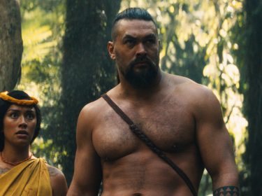 Auf dem Bild aus der Serie Chief of War ist Jason Momoa in einer zentralen Szene im Dschungel zu sehen. Er steht oberkörperfrei neben einer weiteren Figur, beide wirken angespannt und fokussiert. Die Szene ist atmosphärisch dicht, mit dramatischer Beleuchtung im tropischen Wald. Ideal für Fans von Jason Momoas beste Filme und Serien.