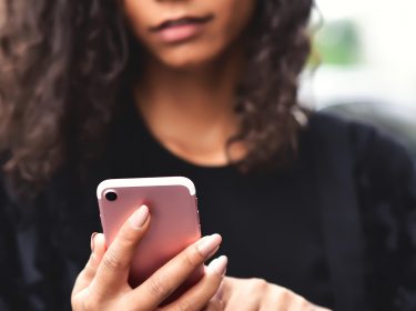 Frau mit Locken guckt auf ihr iPhone SE