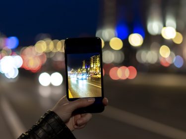 Frau macht mit dem Smartphone ein Foto bei Nacht