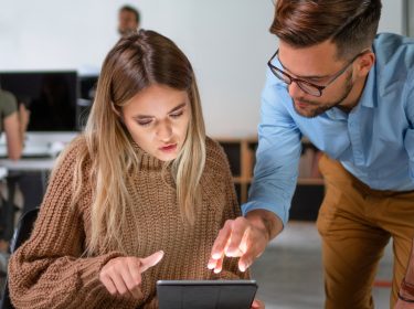 Ein junger Mann und eine jungen Frau im Büro sehen sich etwas auf dem Tablet an.