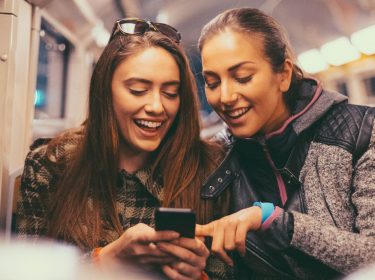 Zwei junge Frauen in der Bahn schauen gemeinsam auf ein Smartphone