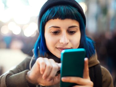 Eine junge Frau tippt auf ihrem Smartphone.