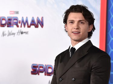 Tom Holland beste Filme – auf diesem Bild ist Tom Holland bei der Premiere von Spider-Man: No Way Home zu sehen. Er trägt einen eleganten, dunkelbraunen Anzug mit schwarzer Krawatte und blickt leicht lächelnd in die Kamera.
