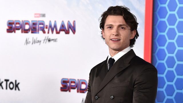 Tom Holland beste Filme – auf diesem Bild ist Tom Holland bei der Premiere von Spider-Man: No Way Home zu sehen. Er trägt einen eleganten, dunkelbraunen Anzug mit schwarzer Krawatte und blickt leicht lächelnd in die Kamera.
